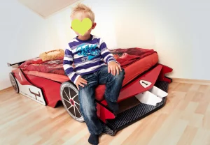 Personenfotograf zuhause - Portrait-Foto eines kleinen Jungen beim Fotoshooting zuhause mit einem Fotograf im Kinderzimmer mit seinem Rennwagen-Bett
