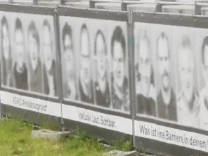 Ein Banner auf einem Gerüst mit 4 Gesichtern, welche digital anonymisiert wurden. Darunter die Worte 