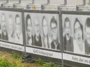 Banner an einem Gerüst. 4 Gesichter, welche digital anonymisiert wurden. Darunter steht 