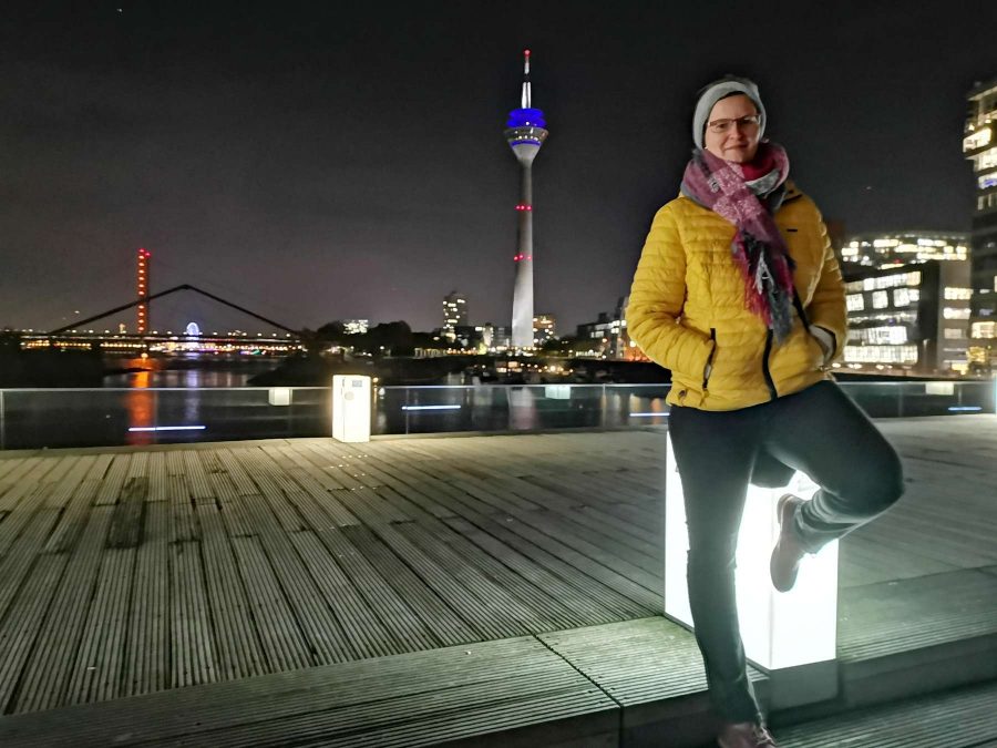 Hübsche Frau bei einem Fotoshooting mit Fotograf Rainer Rössler im abendlichen Düsseldorf auf der Brücke im Medienhafen. Im Hintergrund sind die Lichter der Stadt zu sehen.