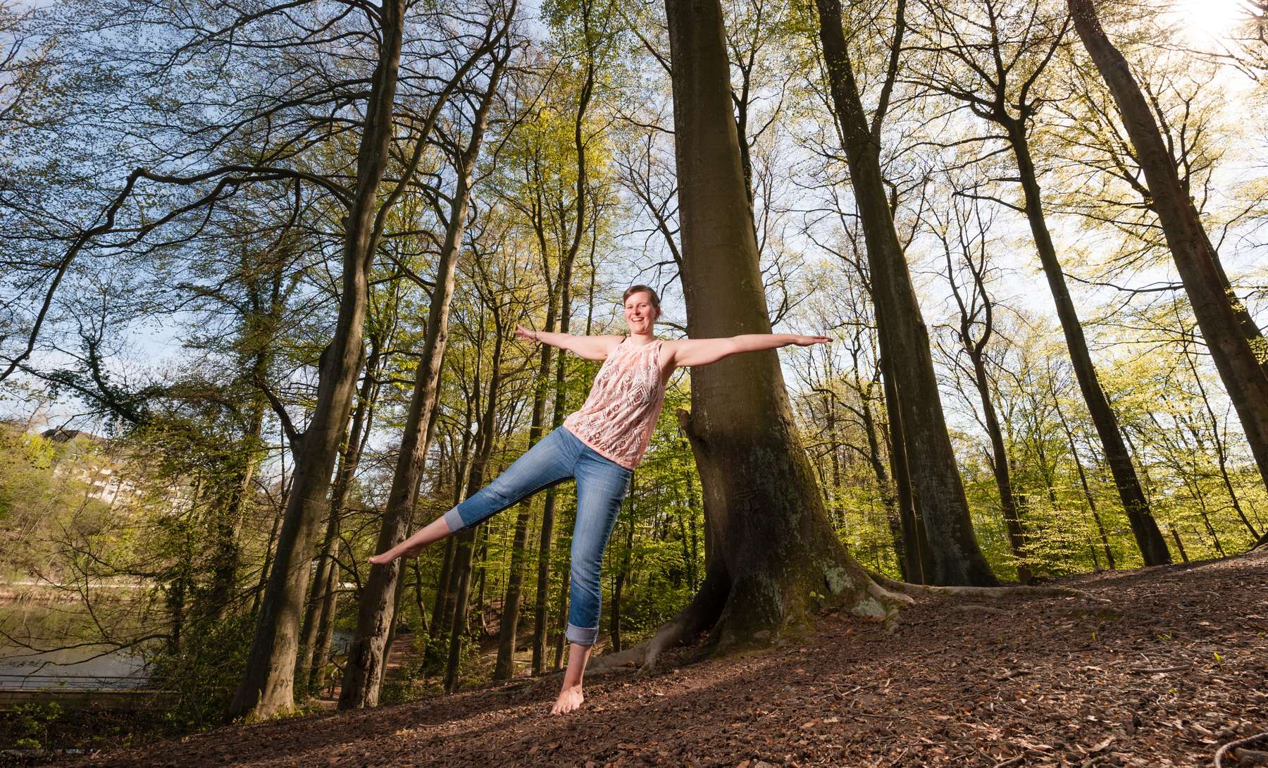 Personenfotograf Essen - Dynamisches Frühlings-Fotoshooting mit Barfuß-Balance-Übung einer jungen Frau im grünen Stadtwald der Margarethenhöhe inmitten der Stadt Essen