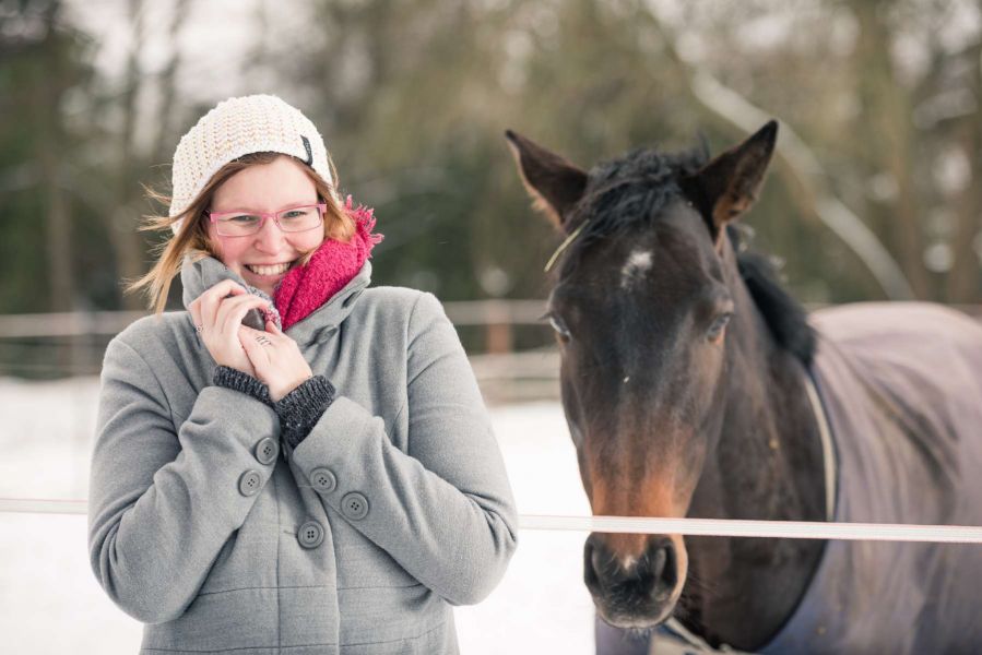Junge hübsche Frau lächelt trotz Kälte am verschneiten Tag mit Ihrem Pferd um die Wette