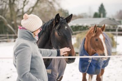 Hübsche Frau genießt Ihre Freizeit an einem verschneiten Tag mit Ihren Pferden.